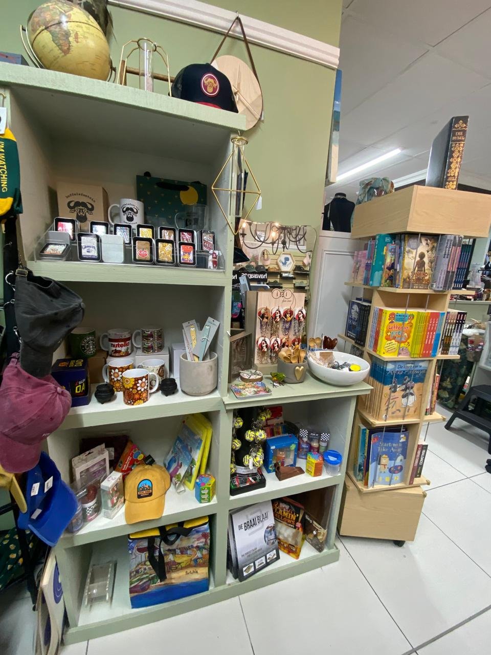 Sage-green shelving at Mooi filled with mugs, caps, novelty gifts and the book spinner
